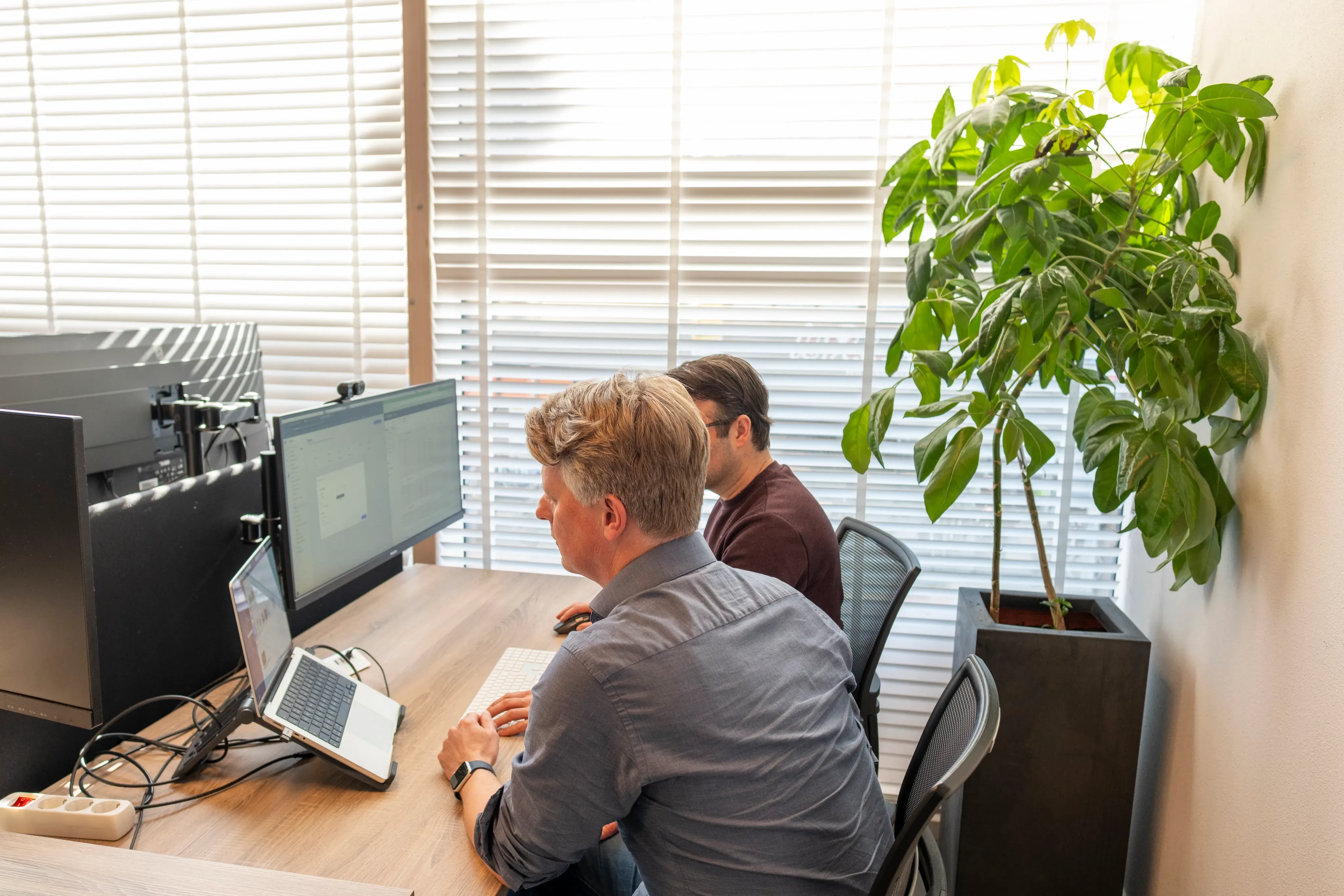 Twee mannen werken samen aan bureaus met laptops en schermen
